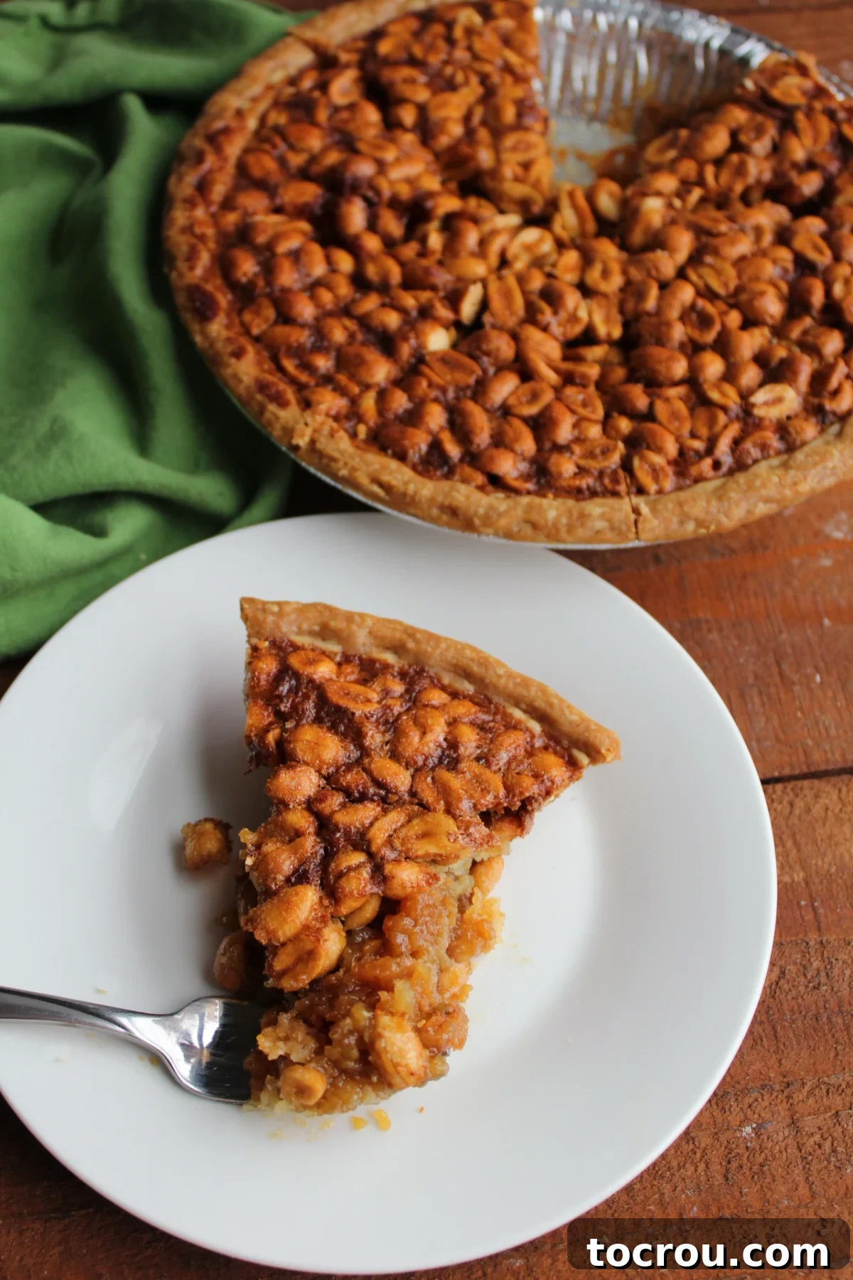 Fork lifting a bite of peanut pie, revealing the luscious gooey brown sugar filling and the appealing crunch of roasted peanuts on top.