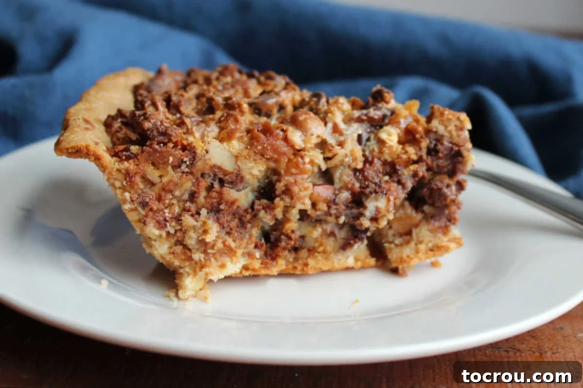 Magic Cookie Bar Pie Slice A close-up shot of a perfect slice of Magic Cookie Bar Pie, showcasing its traditional pie crust generously filled with layers of coconut, pecans, chocolate, gooey caramel, and crunchy pretzel bits. The texture is invitingly soft and chewy.