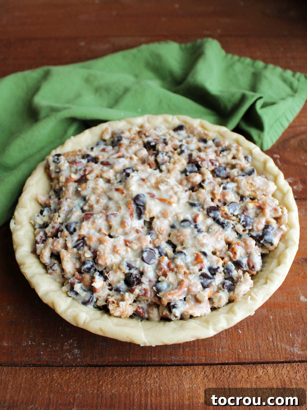 Magic Cookie Bar Pie Before Baking A deep-dish pie crust, generously filled with a thick, golden mixture of sweetened condensed milk, shredded coconut, caramel bits, rich chocolate chips, graham crackers, and pretzels, perfectly prepped and ready for baking in the oven.