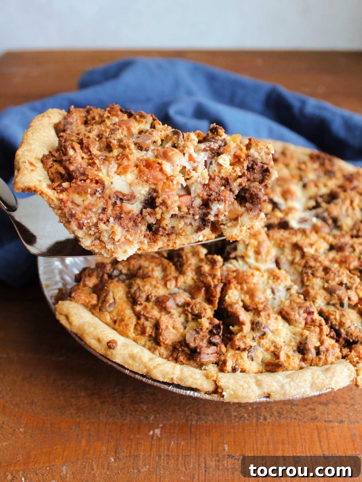 Serving Magic Cookie Bar Pie A hand lifting a perfectly baked and cooled slice of Magic Cookie Bar Pie out of the pie dish, revealing its thick, rich filling and golden-brown crust.