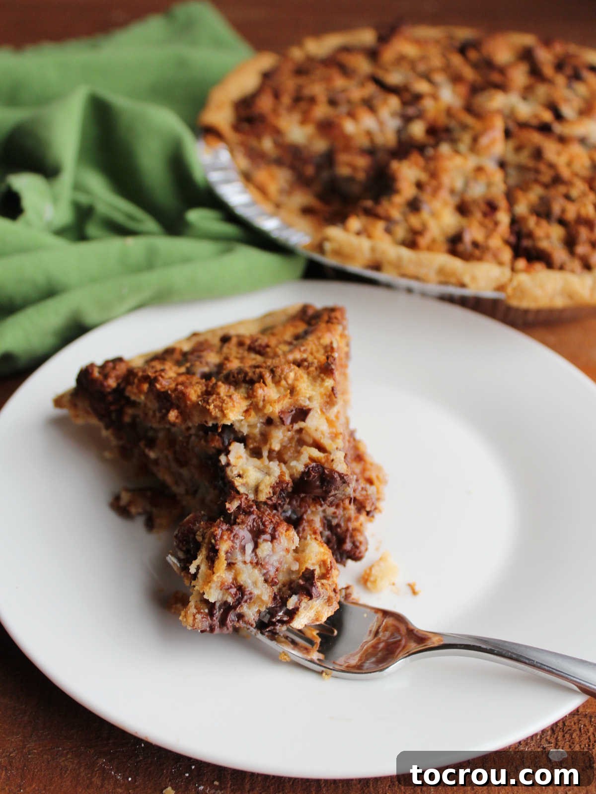 Magic Cookie Bar Pie Bite A close-up of a bite of Magic Cookie Bar Pie on a fork, showing the decadent filling packed with shredded coconut, glistening melted chocolate, crunchy pecans, and other sweet and savory elements.