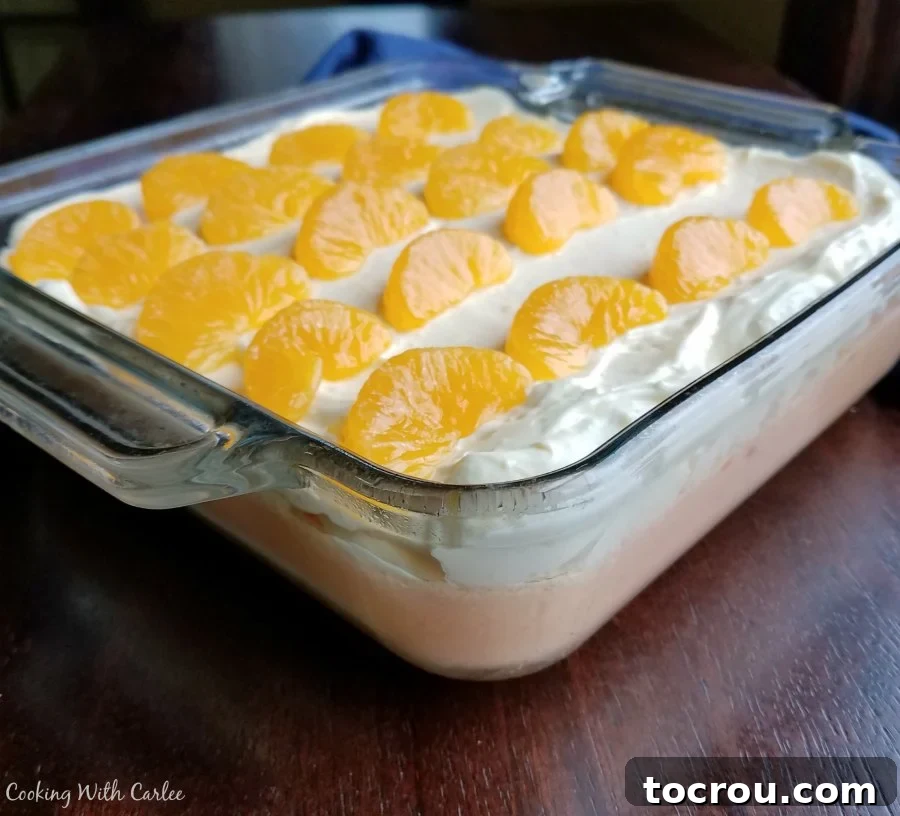 Sunshine Creamsicle Swirl 4 A pan of creamy orange jello, generously topped with fluffy vanilla pudding and vibrant orange slices, ready to be served.