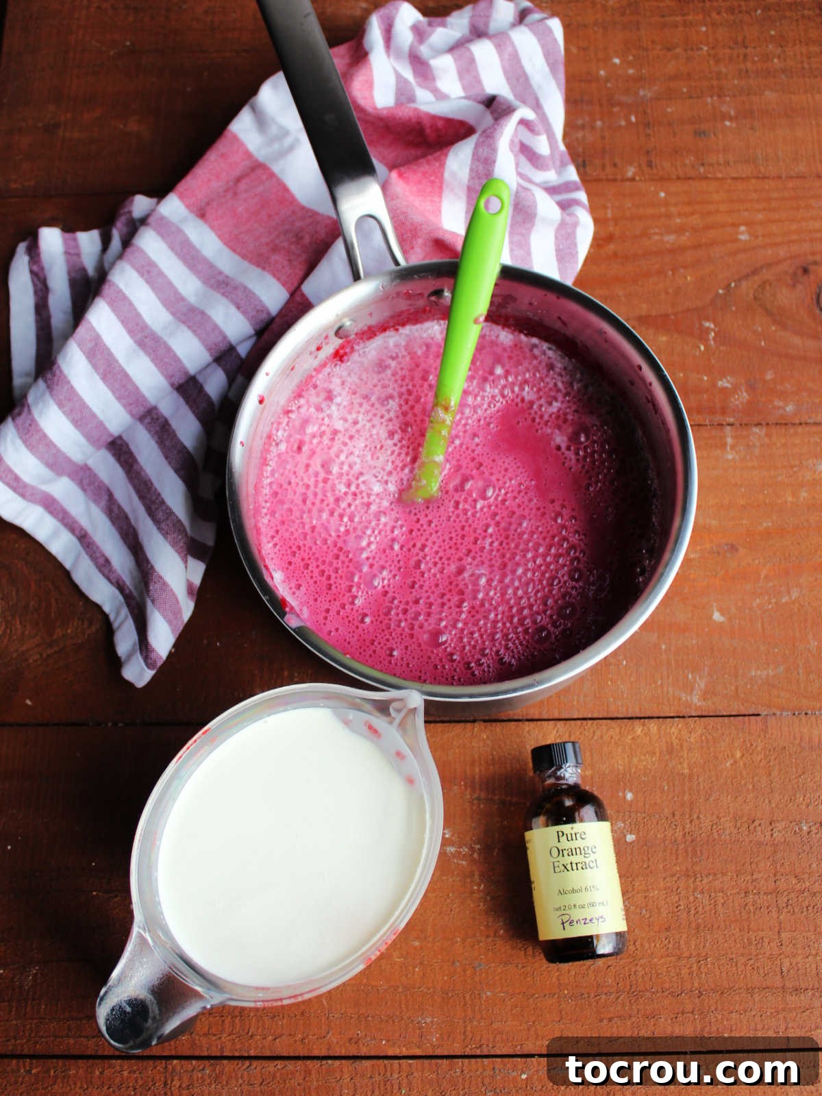Crimson Cranberry Chill 5 Saucepan after cranberry sauce has been processed smooth and milk has been stirred in next to measuring cup with heavy cream and bottle of orange extract.