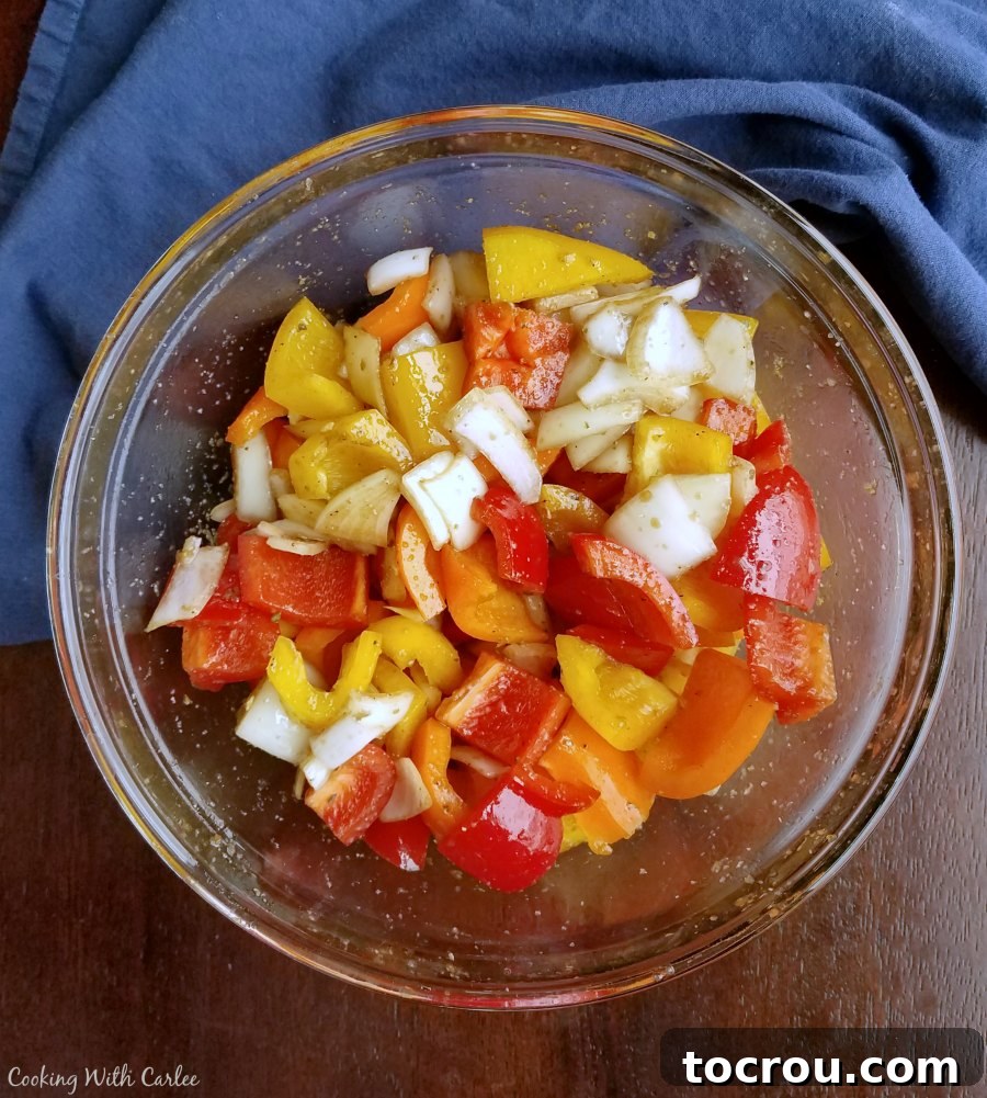 Freshly chopped bell peppers and onions marinated in a savory herb and oil mixture for perfect roasting. A bowl filled with vibrant chunks of bell peppers and onions, glistening with oil and seasonings, ready for roasting.