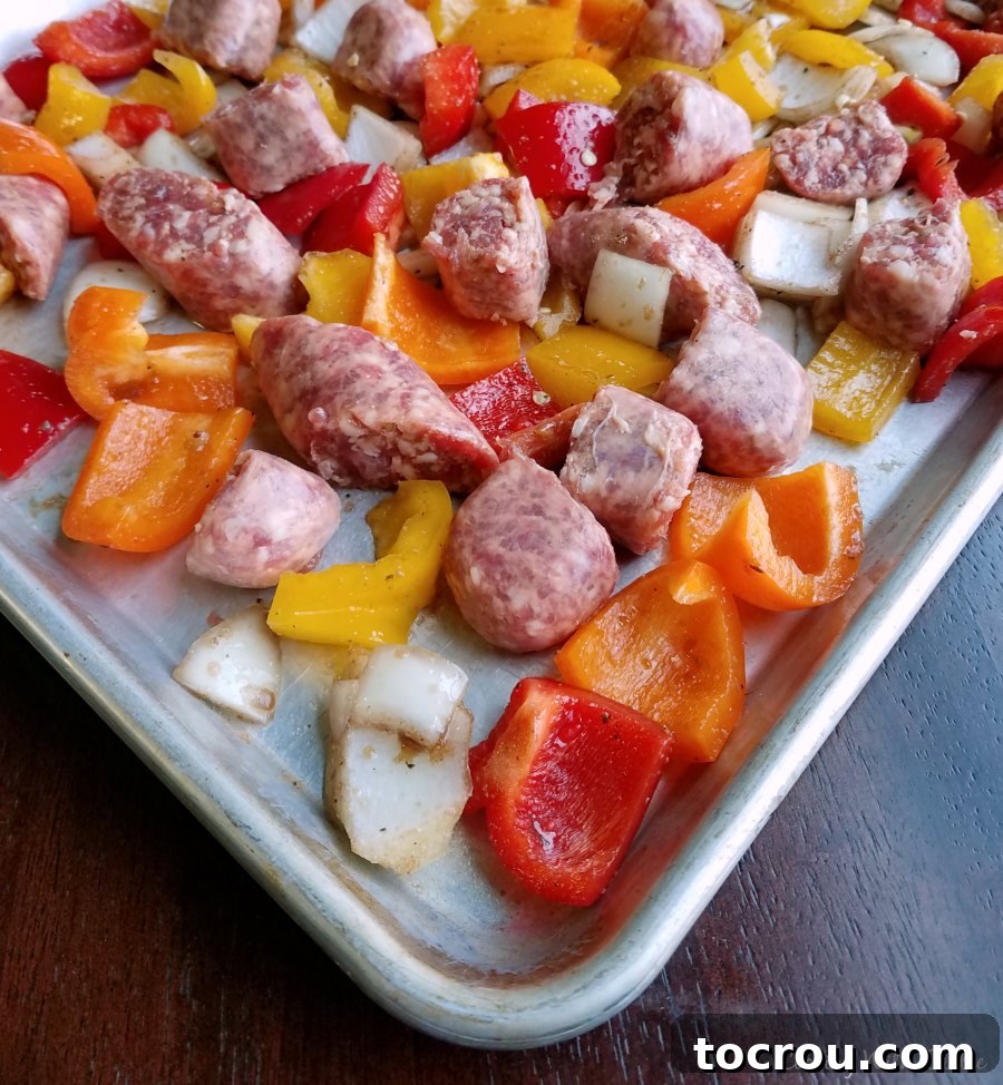 Italian sausage, peppers, and onions, a delicious classic, made effortlessly on a single sheet pan with easy cleanup. Raw chunks of Italian sausage, vibrant bell peppers, and sliced onions spread out on a sheet pan, ready for the oven.
