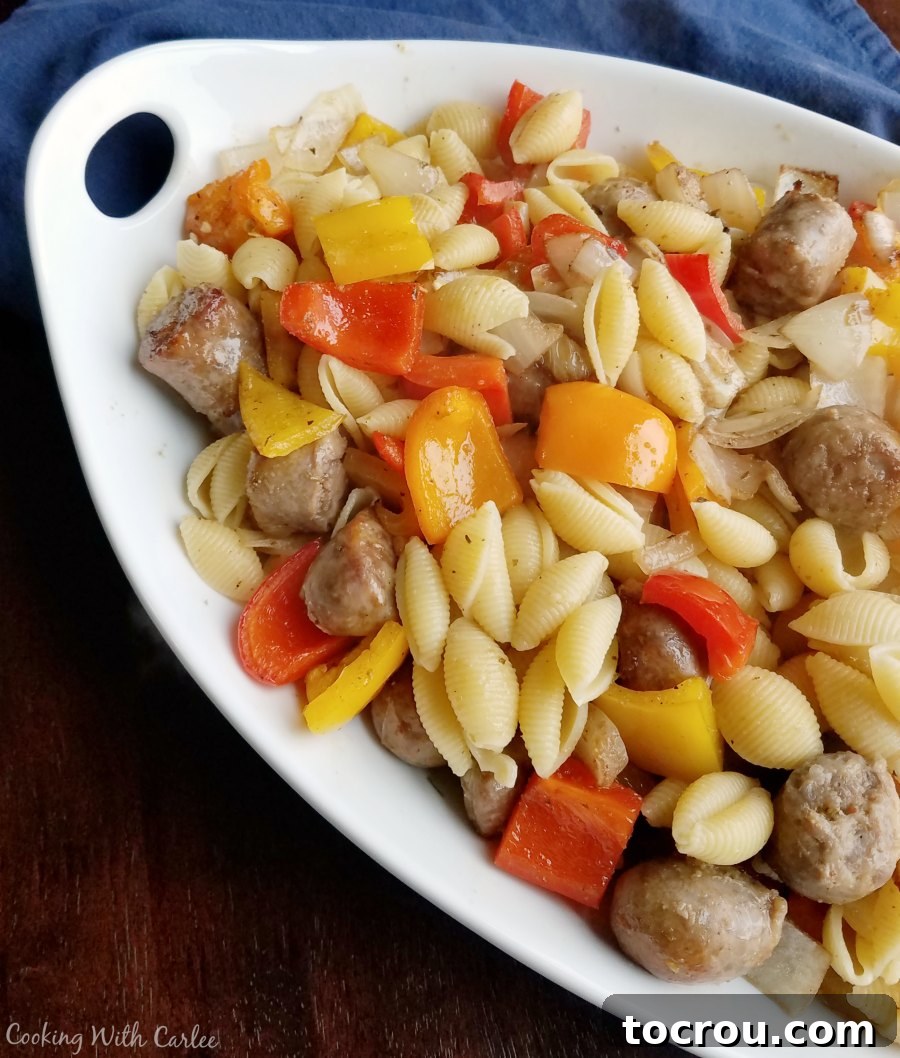A delicious and easy sheet pan dinner: Italian sausage, peppers, and onions mixed with pasta, perfect for a quick and flavorful meal. A large serving dish generously filled with pasta, tossed perfectly with browned Italian sausage, vibrant bell peppers, and caramelized onions.
