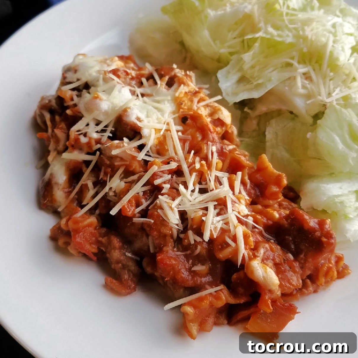 Serving of skillet lasagna with shredded parmesan and salad on a plate.