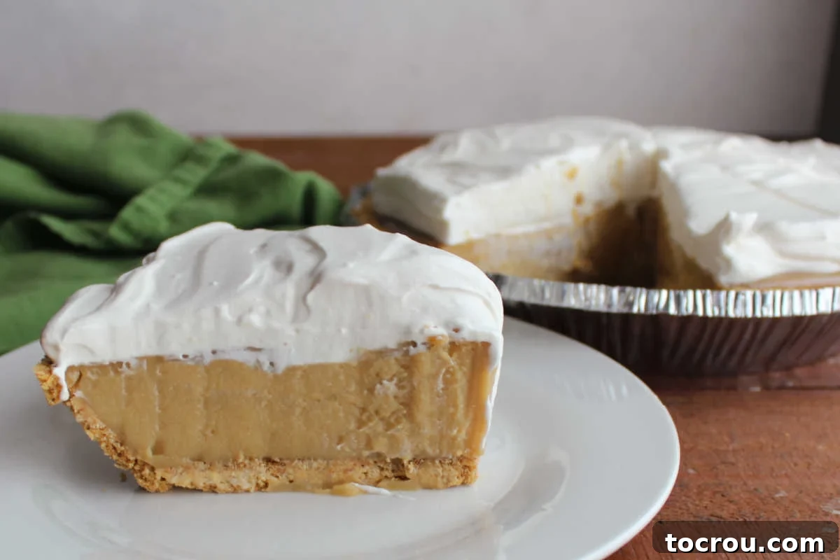 Slice of maple cream pie with creamy maple filling, maple whipped cream topping, and graham cracker crust on plate with remaining pie nearby. 