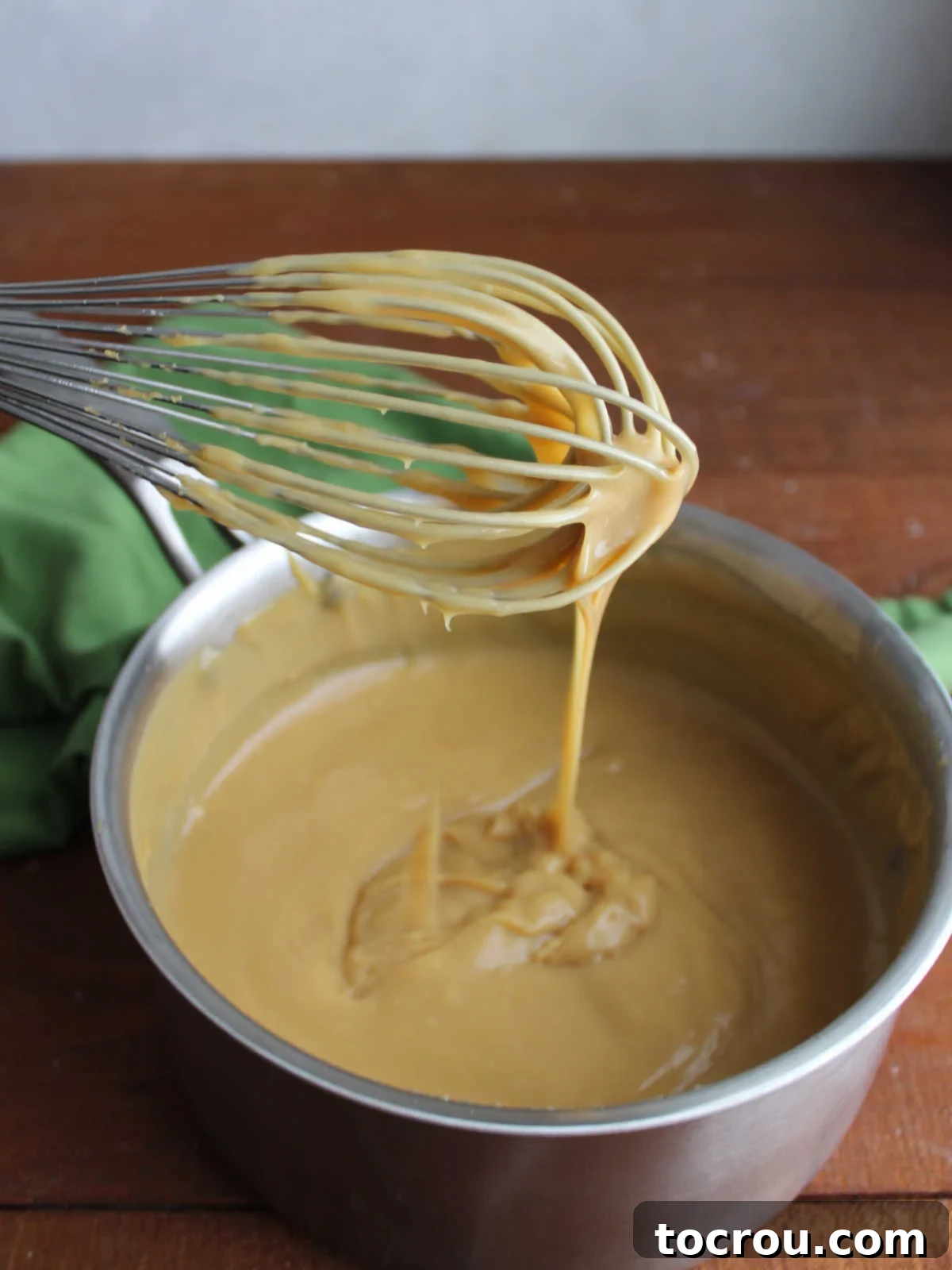 Whisk with thickened maple cream pie filling mixture showing its pudding like texture. 