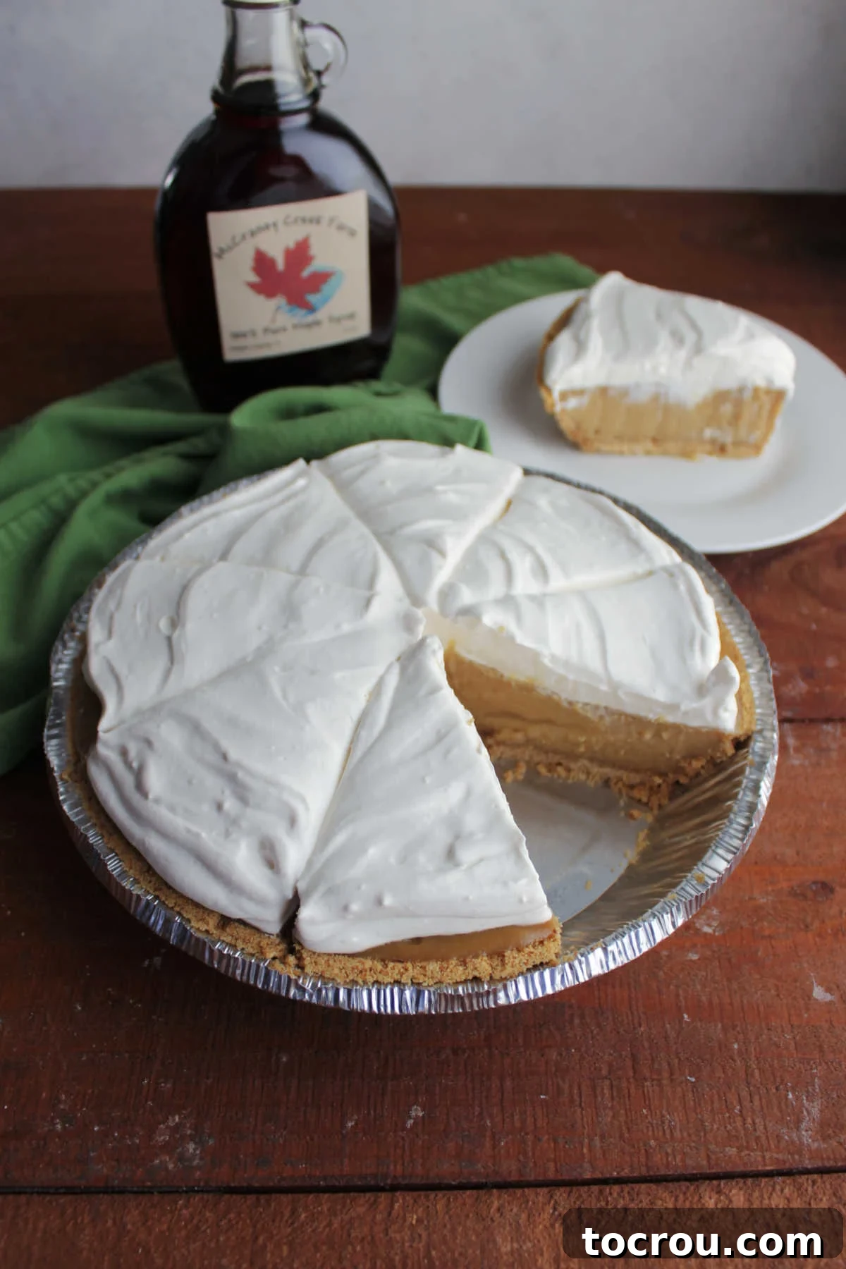 Maple cream pie missing a slice showing thick tan maple filling and fluffy maple cream cheese whipped cream topping. 