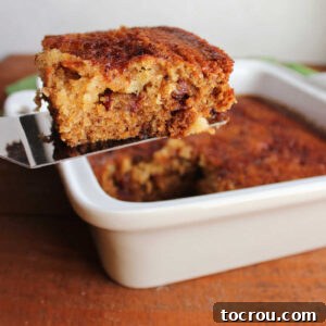 Spatula lifting piece of date pudding out of square baking dish showing bits of date in sticky cake.