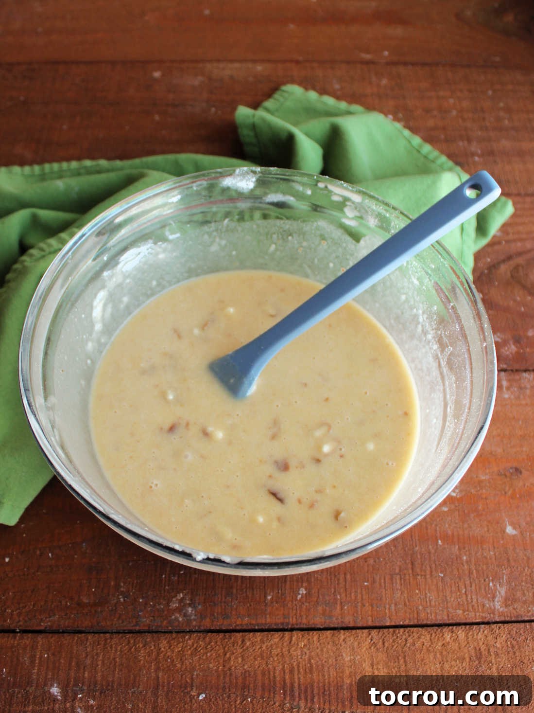 Mixing bowl with date pudding cake batter showing runny texture and bits of dates throughout. 