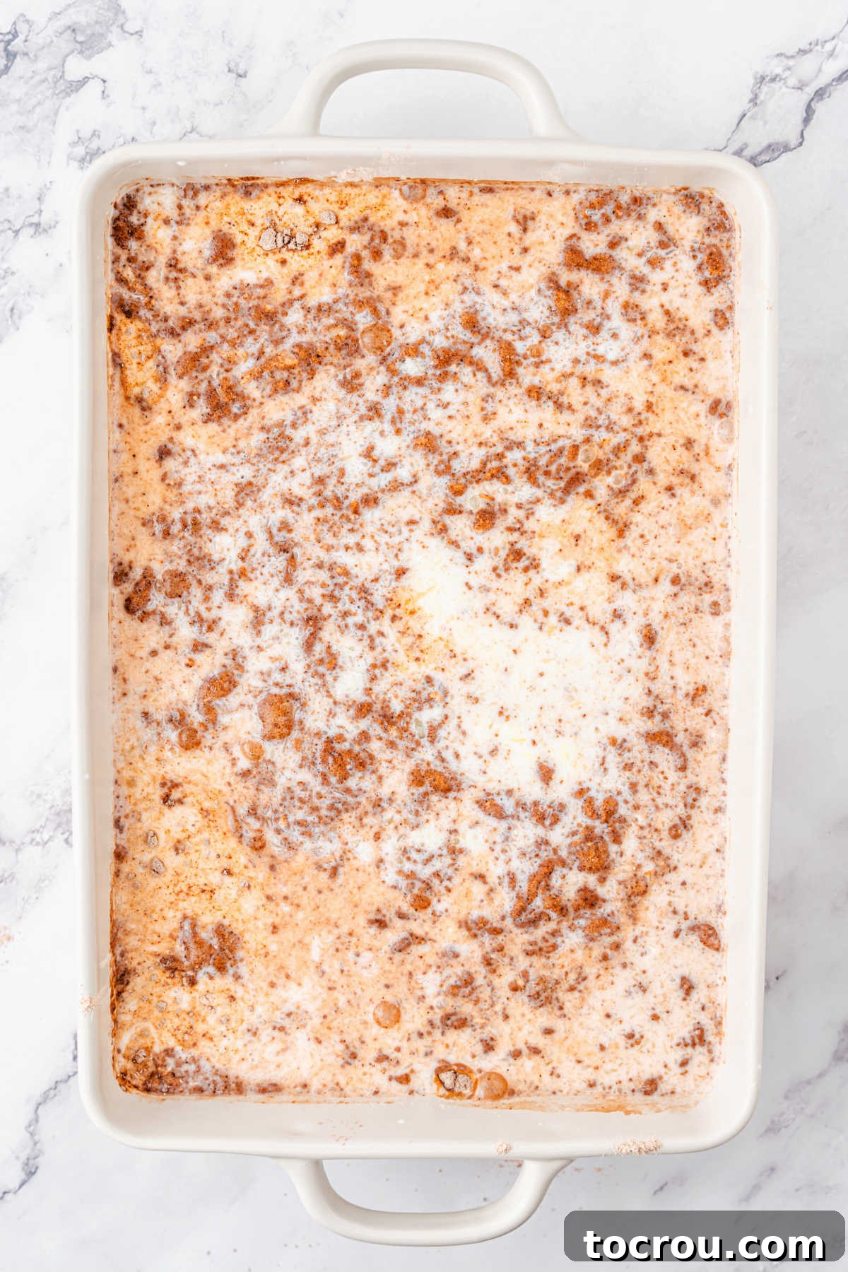 Effortless Chocolate Indulgence 4 Baking dish filled with chocolate cake mix and pudding mixture with butter and milk mixture poured over top, ready to be mixed together.