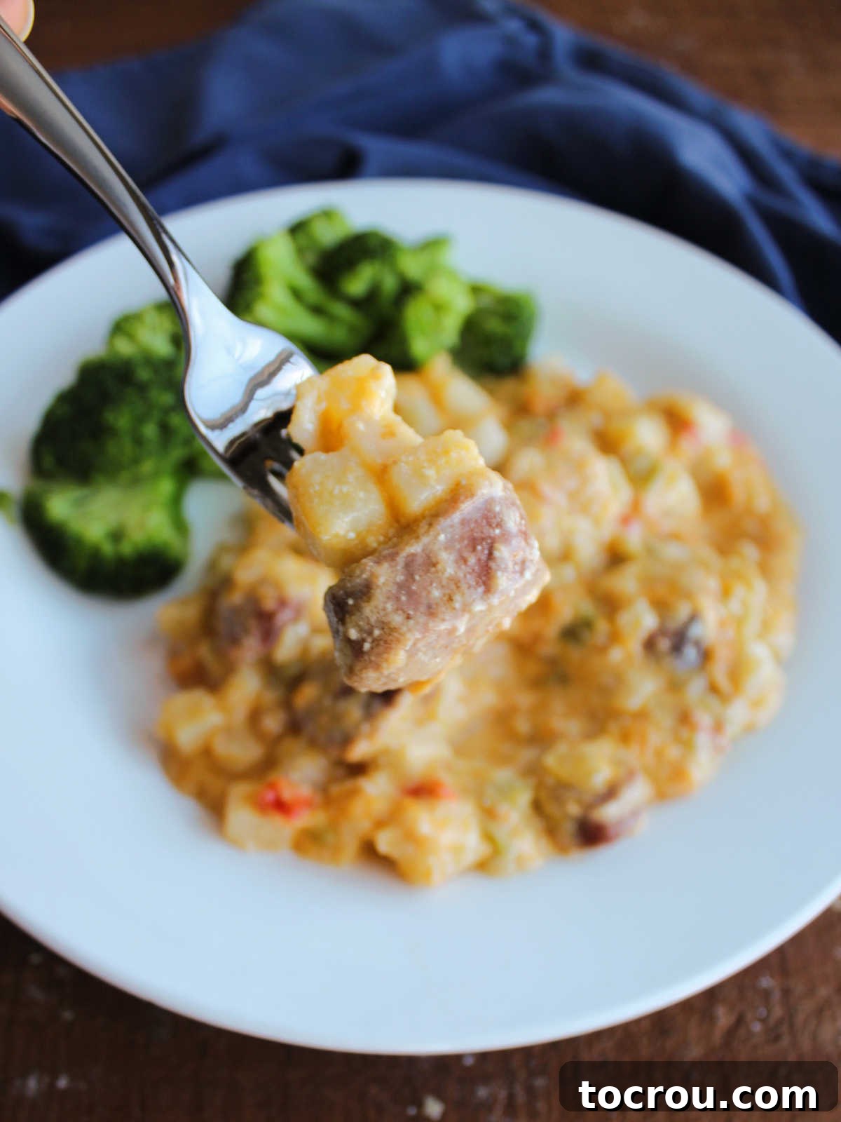 A fork holding a perfect bite of tender potato chunks and savory smoked sausage, drenched in a rich, cheesy sauce, ready to be enjoyed.