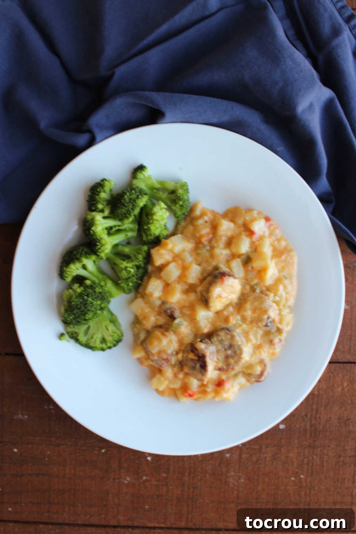 A close-up of a dinner plate featuring a hearty helping of vibrant green steamed broccoli alongside a comforting mound of slow cooker cheesy potatoes and sausage, highlighting the rich textures and appealing colors of a ready-to-eat meal.