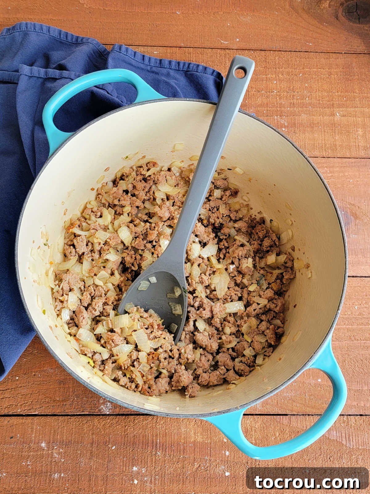 Large enameled cast iron dutch oven with browned Italian sausage and softened diced onion inside, ready to be made into soup. 