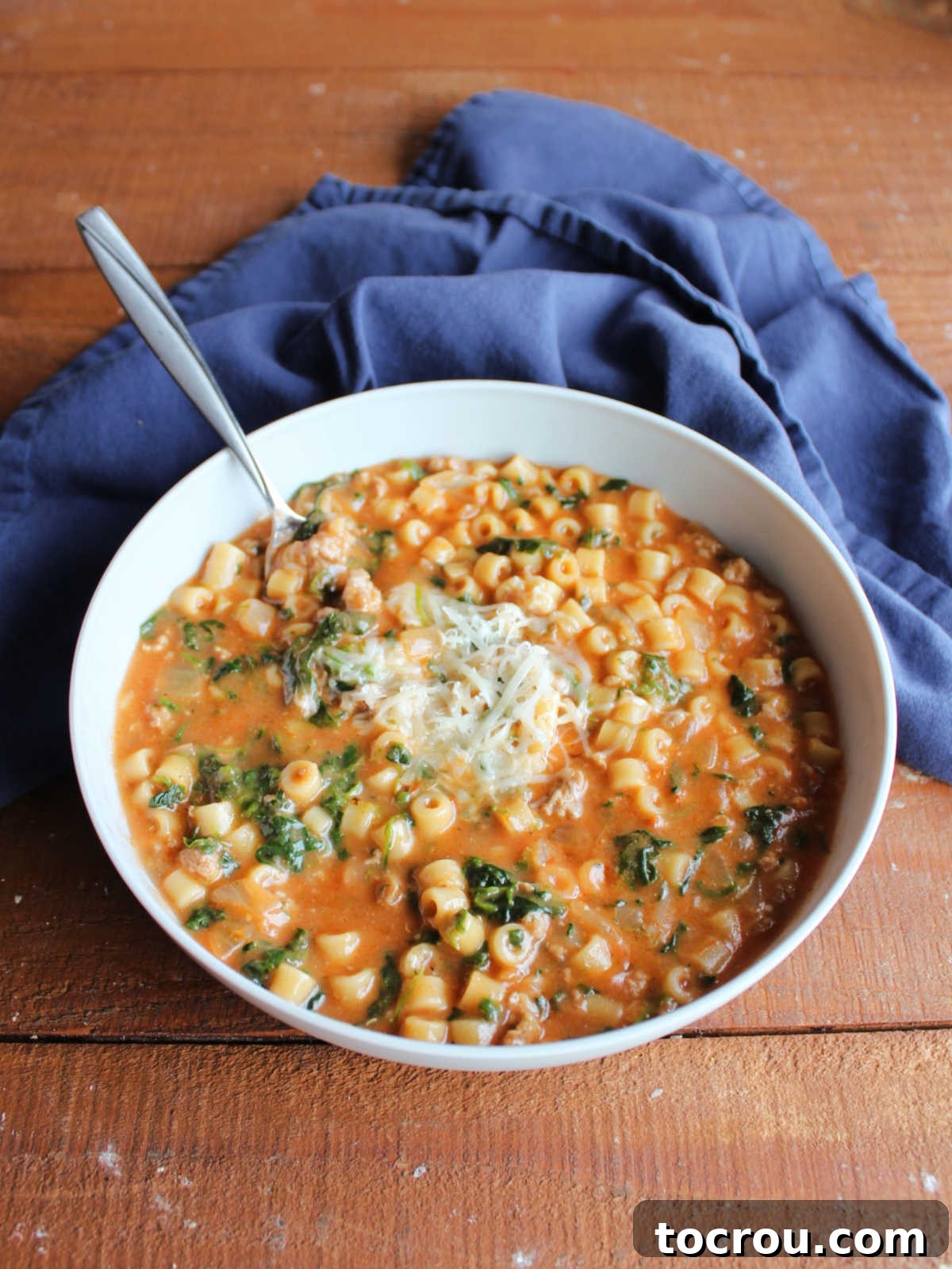 Bowl of Italian soup with sausage, pasta, and spinach in a creamy tomato broth topped with Parmesan cheese, ready to eat. 