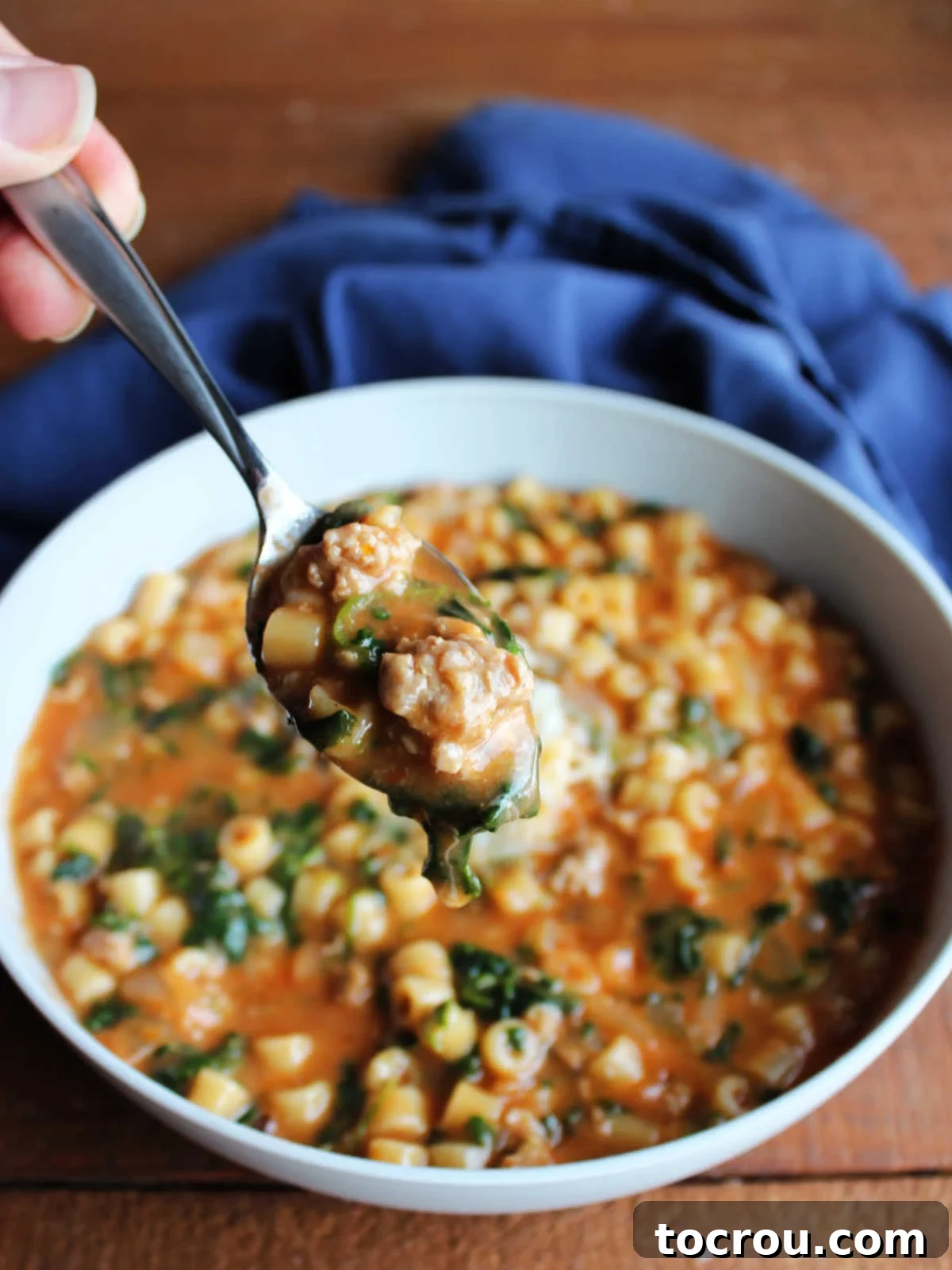 Bite of Italian sausage soup with ditalini pasta and spinach on spoon. 