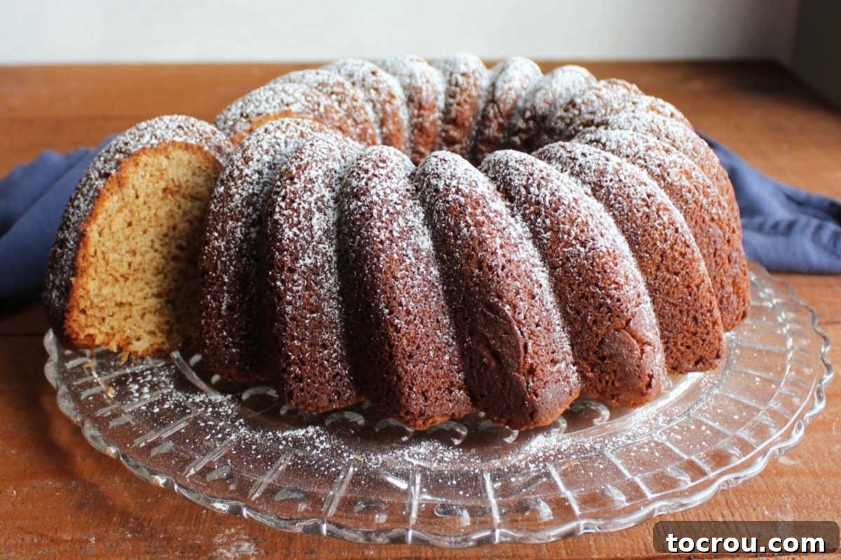 Brown Sugar Pound Cake Slice A perfectly baked slice of brown sugar Bundt cake being gently removed from the whole cake, showcasing its dense, tan interior, small air bubbles, and soft pound cake texture.