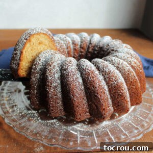 A pristine slice being carefully removed from a brown sugar pound Bundt cake, elegantly dusted with powdered sugar and presented on a vintage glass cake plate.