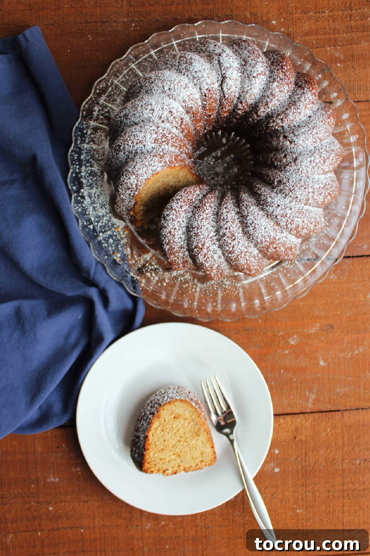 Sliced Pound Cake with Powdered Sugar An overhead view of a delicious slice of brown sugar pound cake served on a plate, positioned beside the elegant Bundt cake, both lightly dusted with powdered sugar.