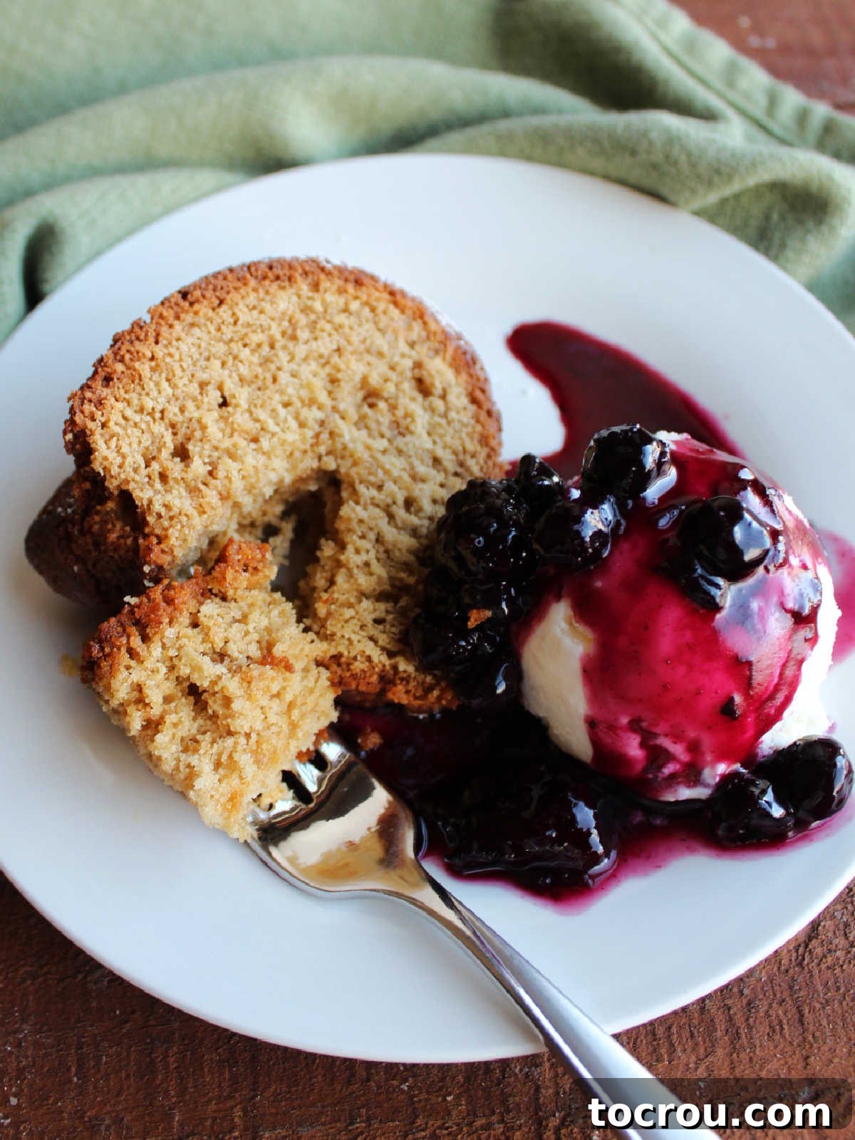 Pound Cake with Ice Cream and Sauce A delightful bite of brown sugar Bundt cake on a fork, with the remaining slice, a scoop of vanilla ice cream, and a vibrant berry sauce in the background.