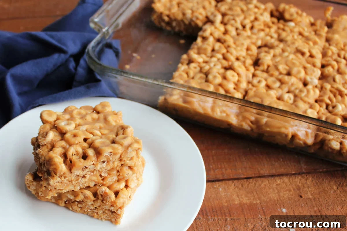 No-Bake Peanut Butter Cheerio Bars A pan full of golden-brown no-bake Cheerio bars, with several perfectly cut squares stacked on a plate nearby, highlighting their chewy texture and peanut butter goodness.