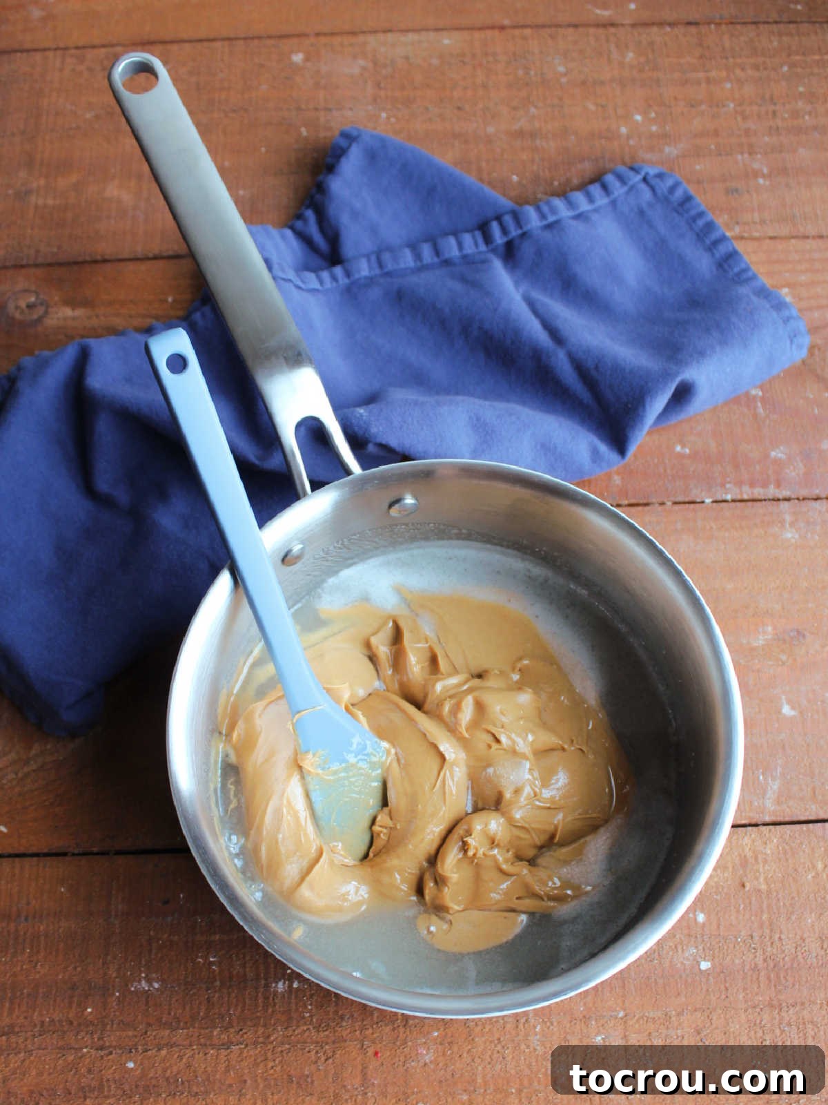 Melting Peanut Butter Mixture A saucepan on a stove with a smooth, glossy peanut butter mixture being stirred, showing the warm blend of sugar, corn syrup, and peanut butter.