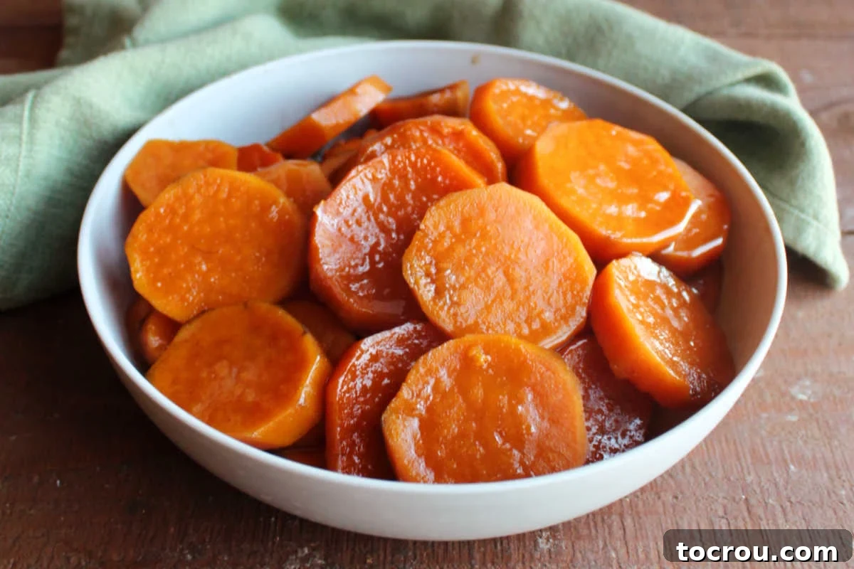 Serving bowl filled with crockpot candied sweet potatoes with thickened brown sugar and cinnamon sauce on them. 