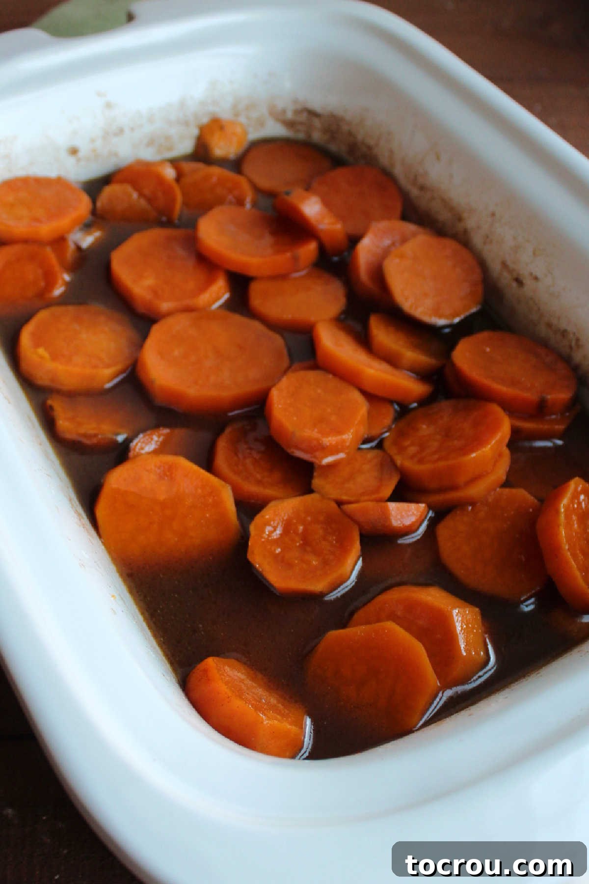 Crockpot filled with cooked sweet potato slices in thickened brown sugar and cinnamon sauce. 