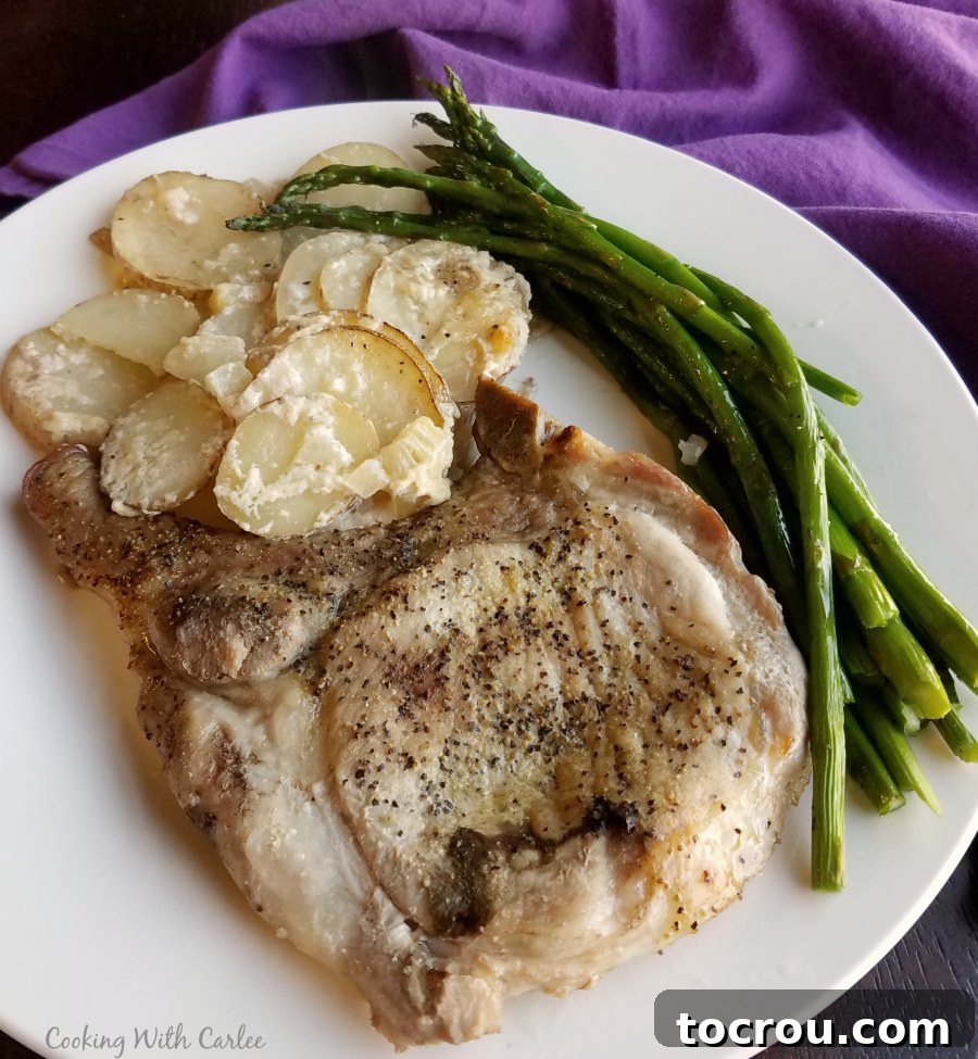 A beautifully plated dinner featuring a golden pork chop, creamy scalloped potatoes, and crisp green asparagus, ready to be served.