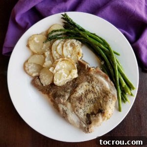 Dinner plate with golden brown scalloped potatoes, a perfectly cooked pork chop, and vibrant green asparagus, ready to be enjoyed.
