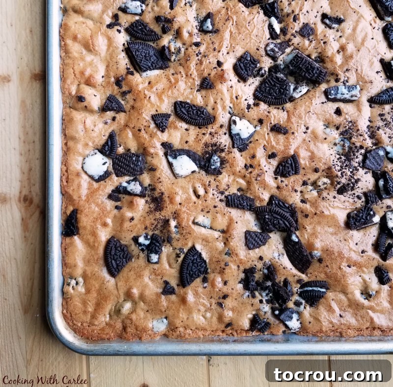 A freshly baked half sheet pan of golden brown Oreo topped blondies, warm from the oven, with a scattering of visible cookie pieces.