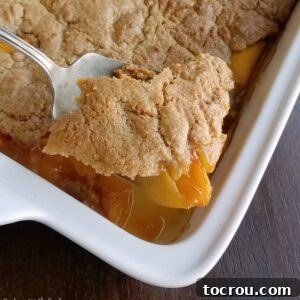 big serving spoon lifting out corner of freshly baked brown sugar peach cobbler.
