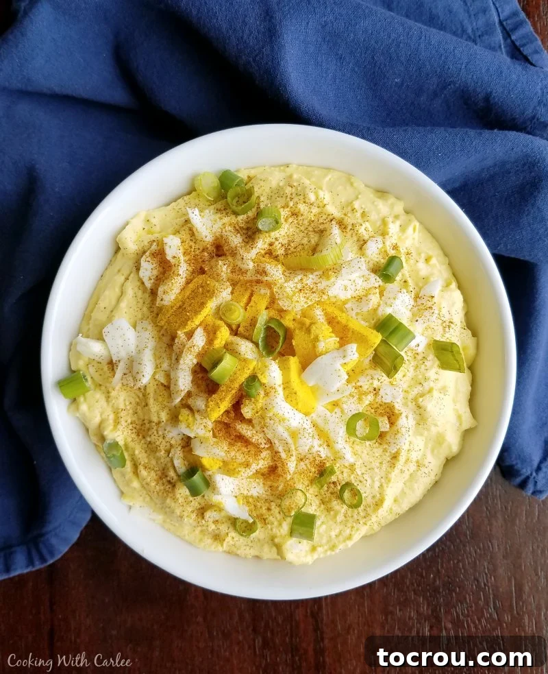 Big bowl of deviled egg dip topped with chopped eggs, green onions and paprika.