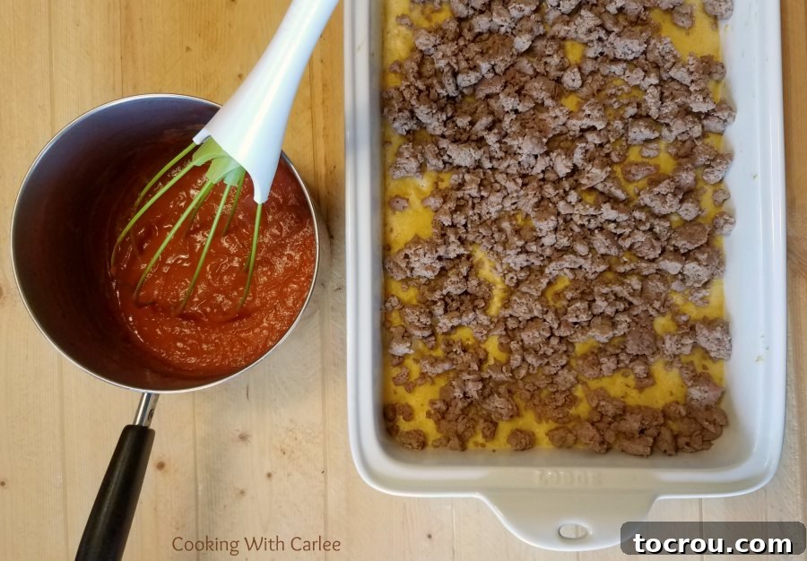 Enchilada Sauce and Seasoned Meat Filling Ready for Layering A rustic saucepan filled with a rich, red enchilada sauce sits invitingly next to a casserole dish, which holds a golden, baked corn base ready for the savory ground meat filling.