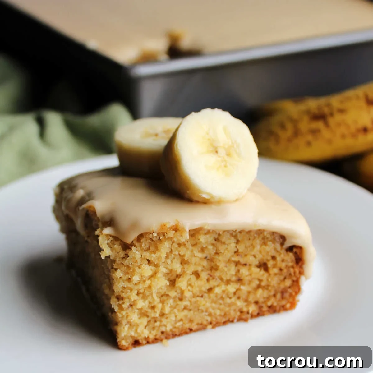 Golden Banana Cake Crowned with Brown Sugar Glaze 2 Square piece of banana cake topped with brown sugar icing and a couple of banana slices, ready to eat.