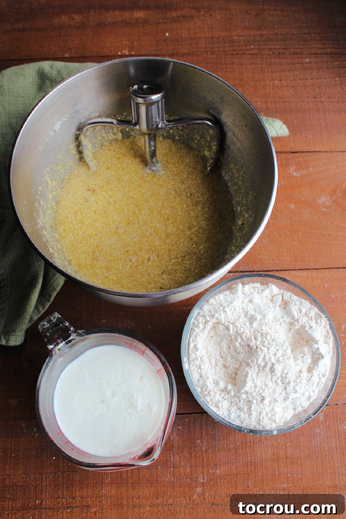 Golden Banana Cake Crowned with Brown Sugar Glaze 5 Mixer bowl with banana, sugar, and butter mixture next to measuring cup with soured milk and bowl of dry ingredients ready to be made into batter.
