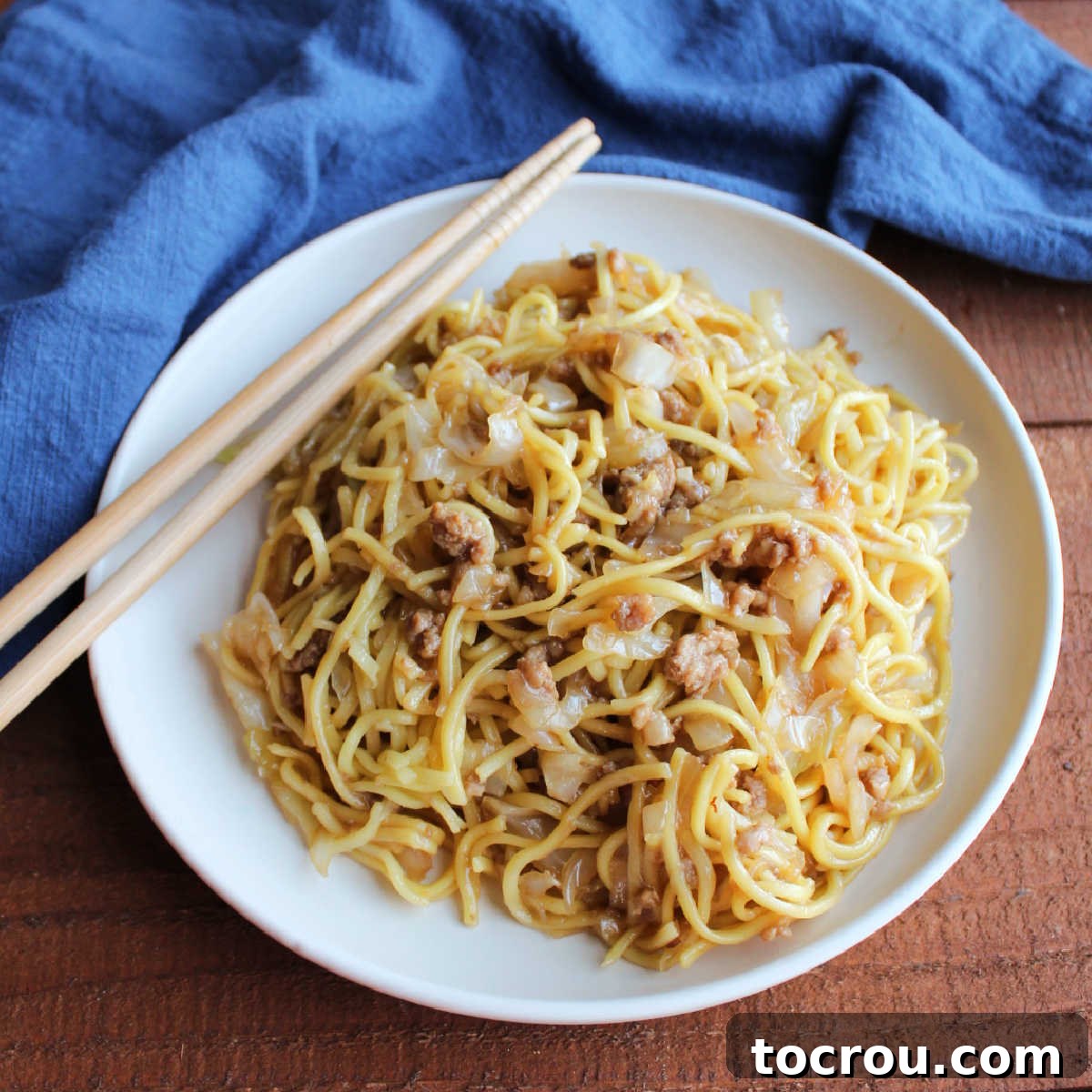 A vibrant plate of pork chow mein noodles, garnished with tender cabbage, seasoned ground pork, and a glossy, light sauce, ready to be enjoyed with chopsticks.