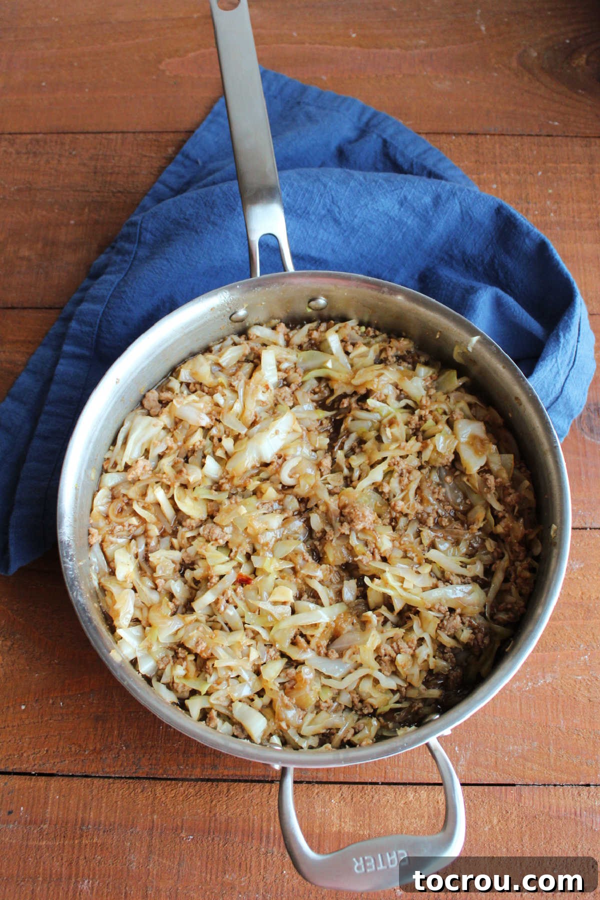 A close-up shot of tender cabbage, sweet onions, and flavorful ground pork, all coated in a rich, Asian-inspired sauce, expertly cooking in a large skillet.