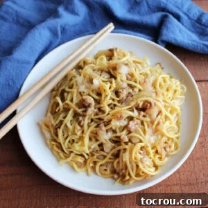 A plate of chow mein noodles with tender cabbage, seasoned ground pork, and a savory sauce, served with chopsticks, ready to eat.