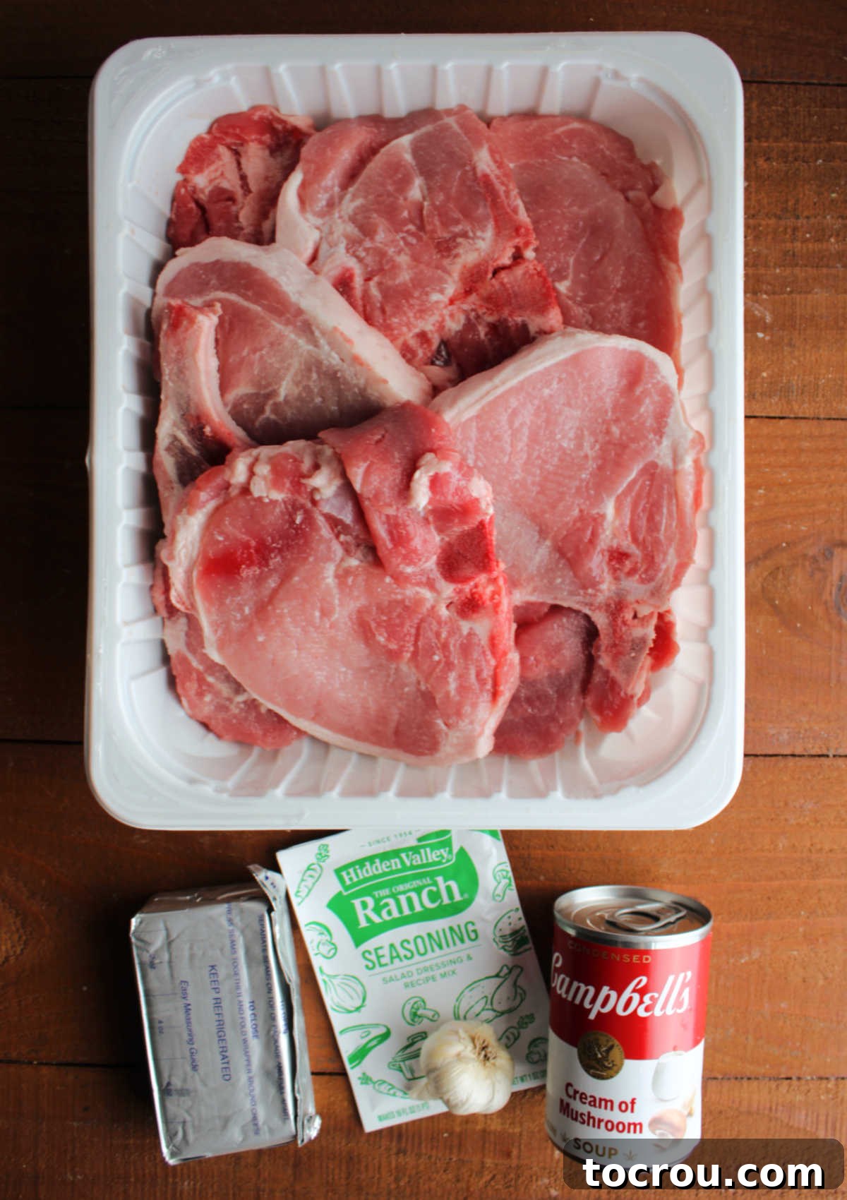 Ingredients for creamy ranch pork chops including a large package of pork chops, a packet of ranch seasoning mix, a can of cream of mushroom soup, cream cheese, and fresh garlic.