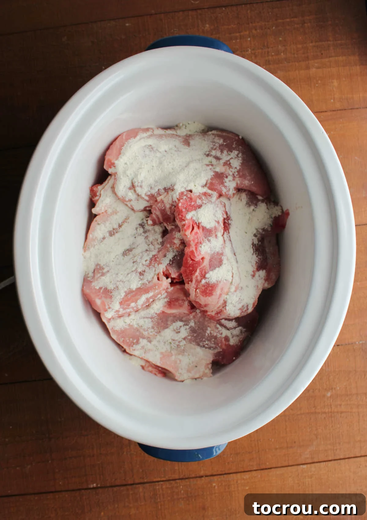 Crockpot with layers of pork chops dusted with ranch seasoning mix, ready for the creamy sauce to be added.