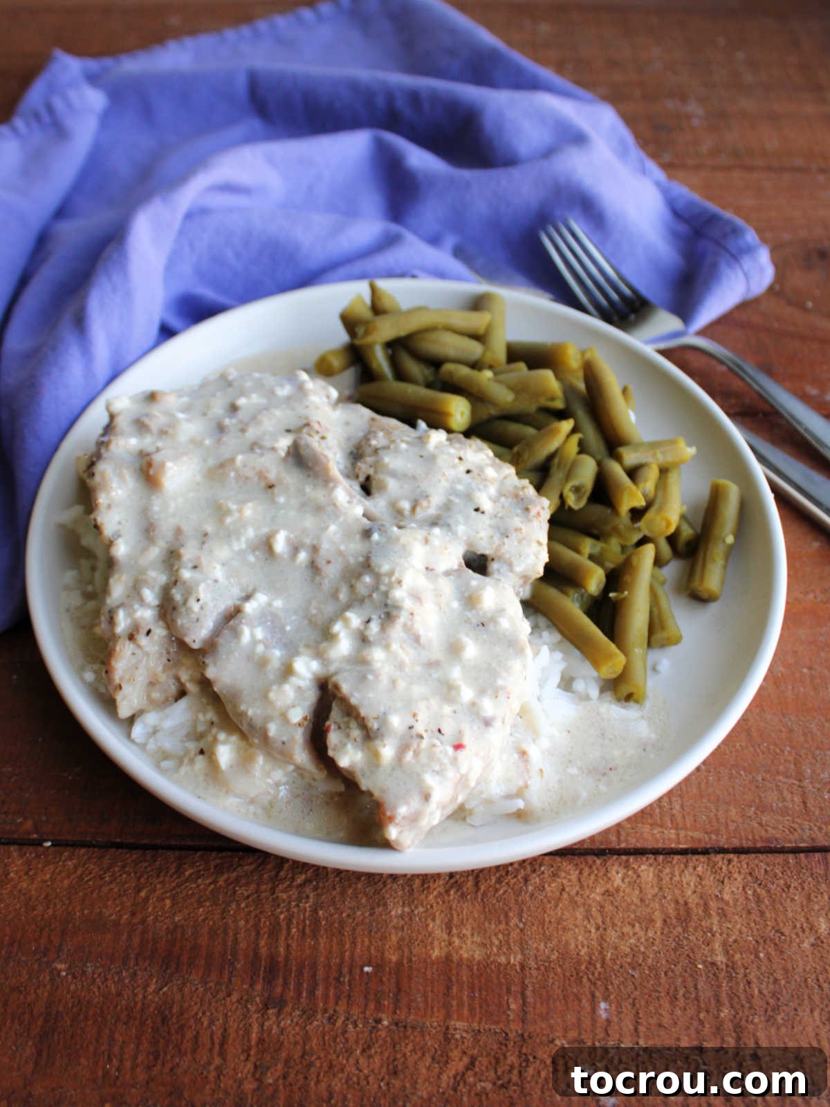 Creamy ranch pork chop served elegantly on a bed of fluffy white rice, accompanied by vibrant green beans, ready for a comforting meal.