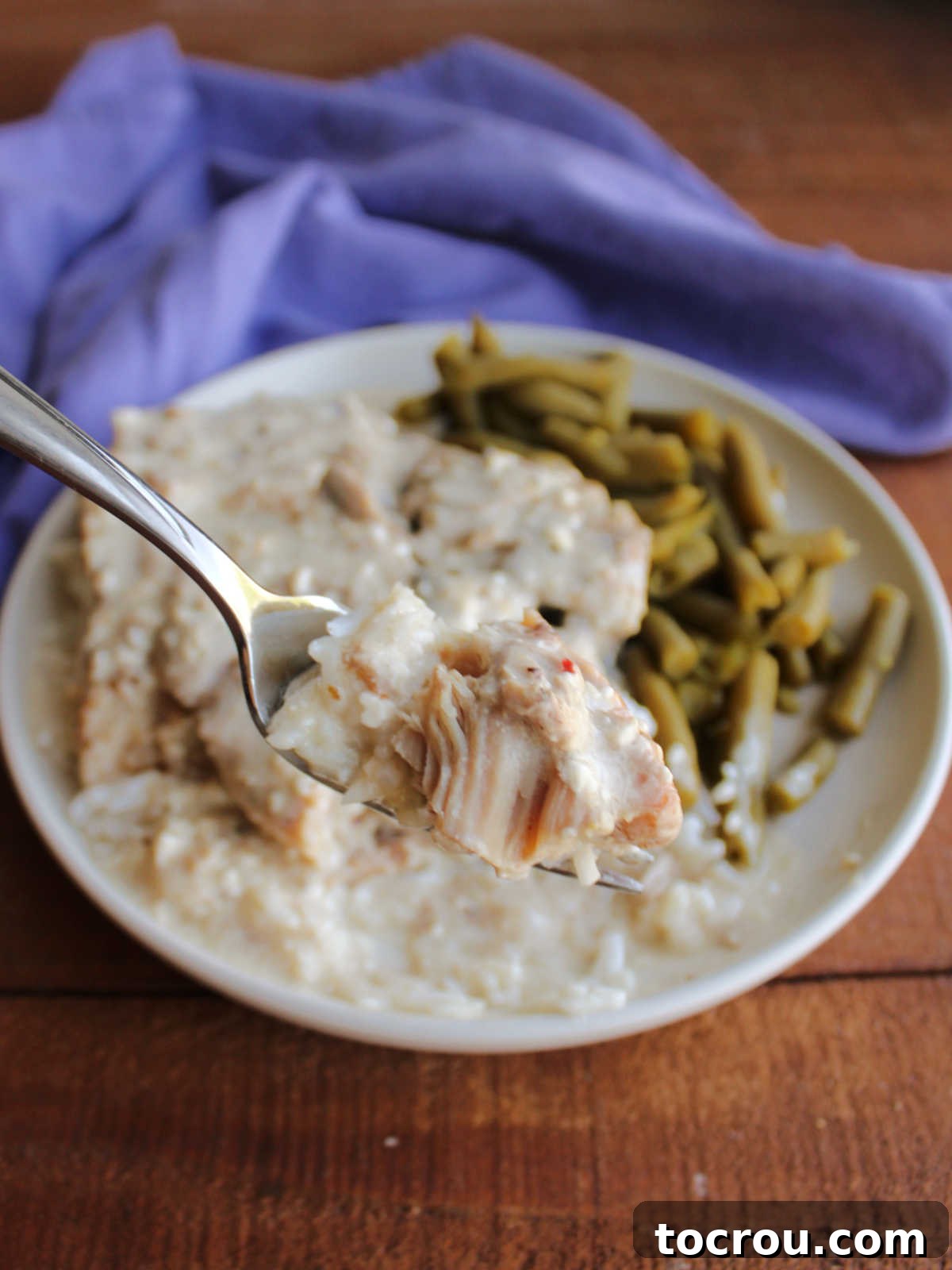 A close-up of a bite of tender pork chop, coated in creamy ranch gravy, on a fork, with the rest of the inviting dinner plate softly blurred in the background.