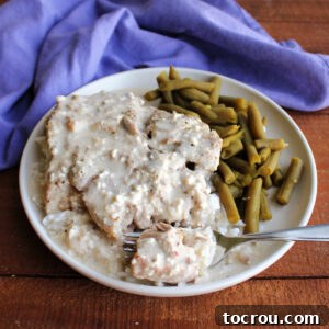 Fork going through tender pork chop in creamy ranch sauce served over rice with a side of green beans.