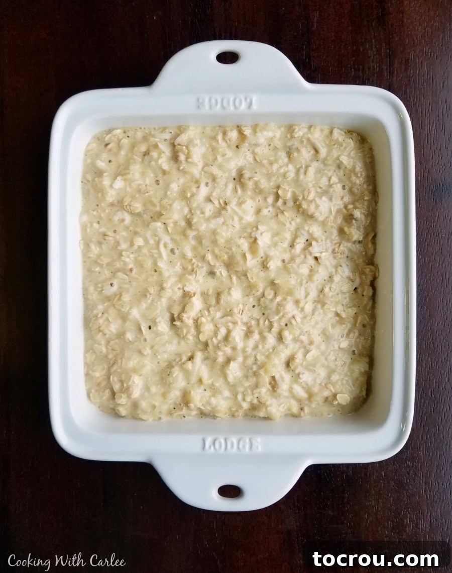 Square baking dish filled with the prepared pineapple and coconut baked oats batter, showcasing the texture and fruit pieces before baking.