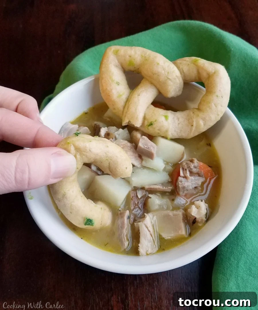 Hand dipping a Celtic knot roll into a bowl of rich, easy chicken stew, showcasing its perfect pairing.