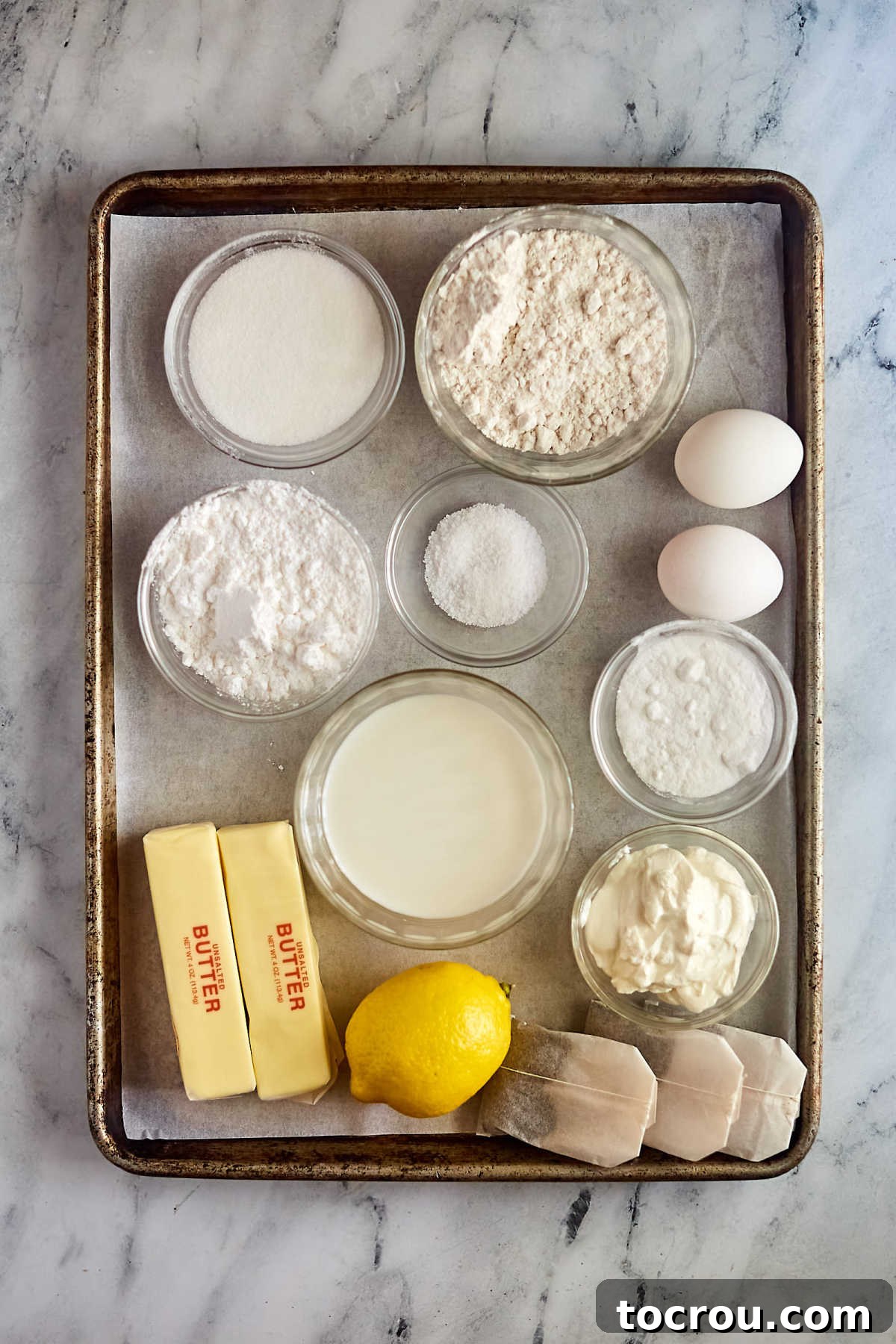 Fresh ingredients laid out for baking a delicious Arnold Palmer Texas Sheet Cake. Ingredients including tea bags, flour, sugar, butter, lemon, sour cream, eggs, milk, powdered sugar etc. ready to be made into arnold palmer sheet cake.