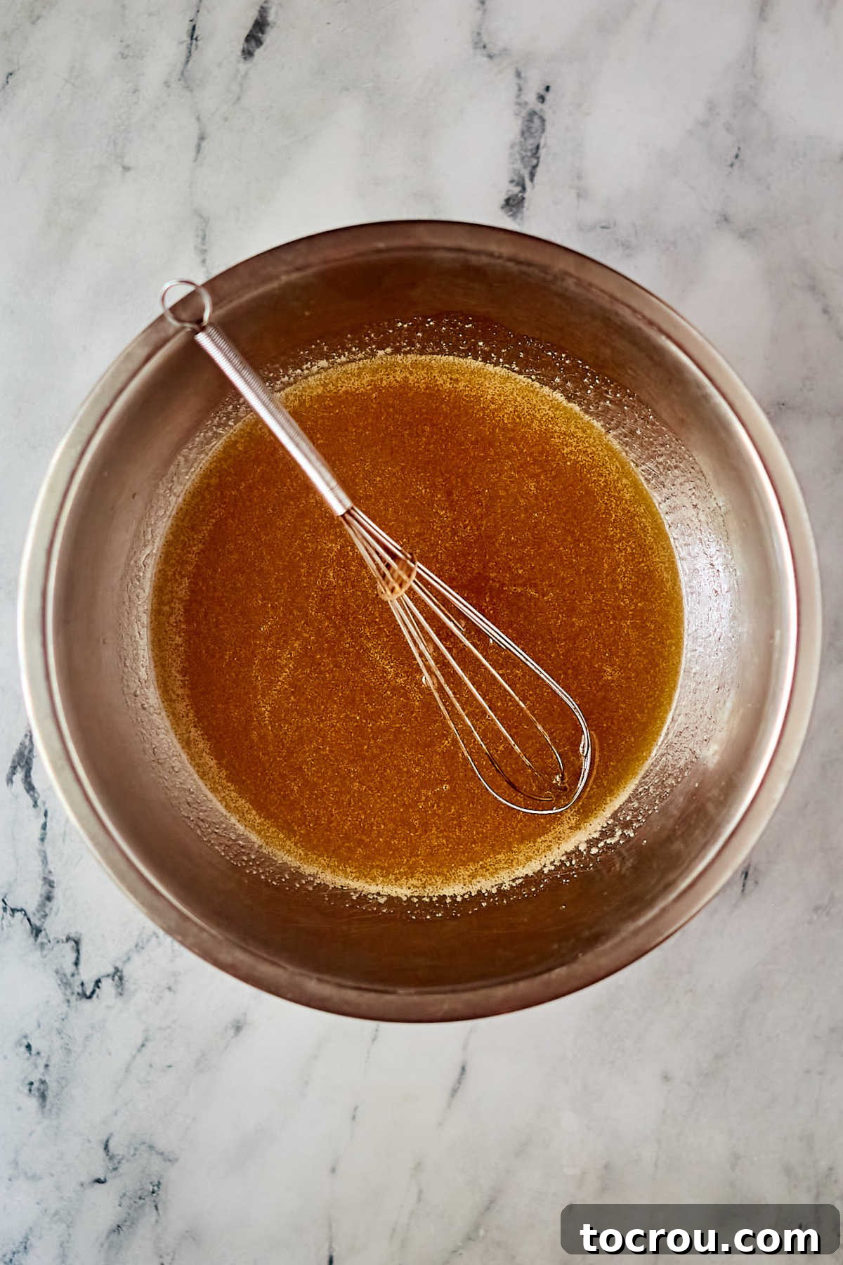 Whisking together the tea-infused cake batter in a large bowl. Large mixing bowl and whisk making tea flavored cake batter.